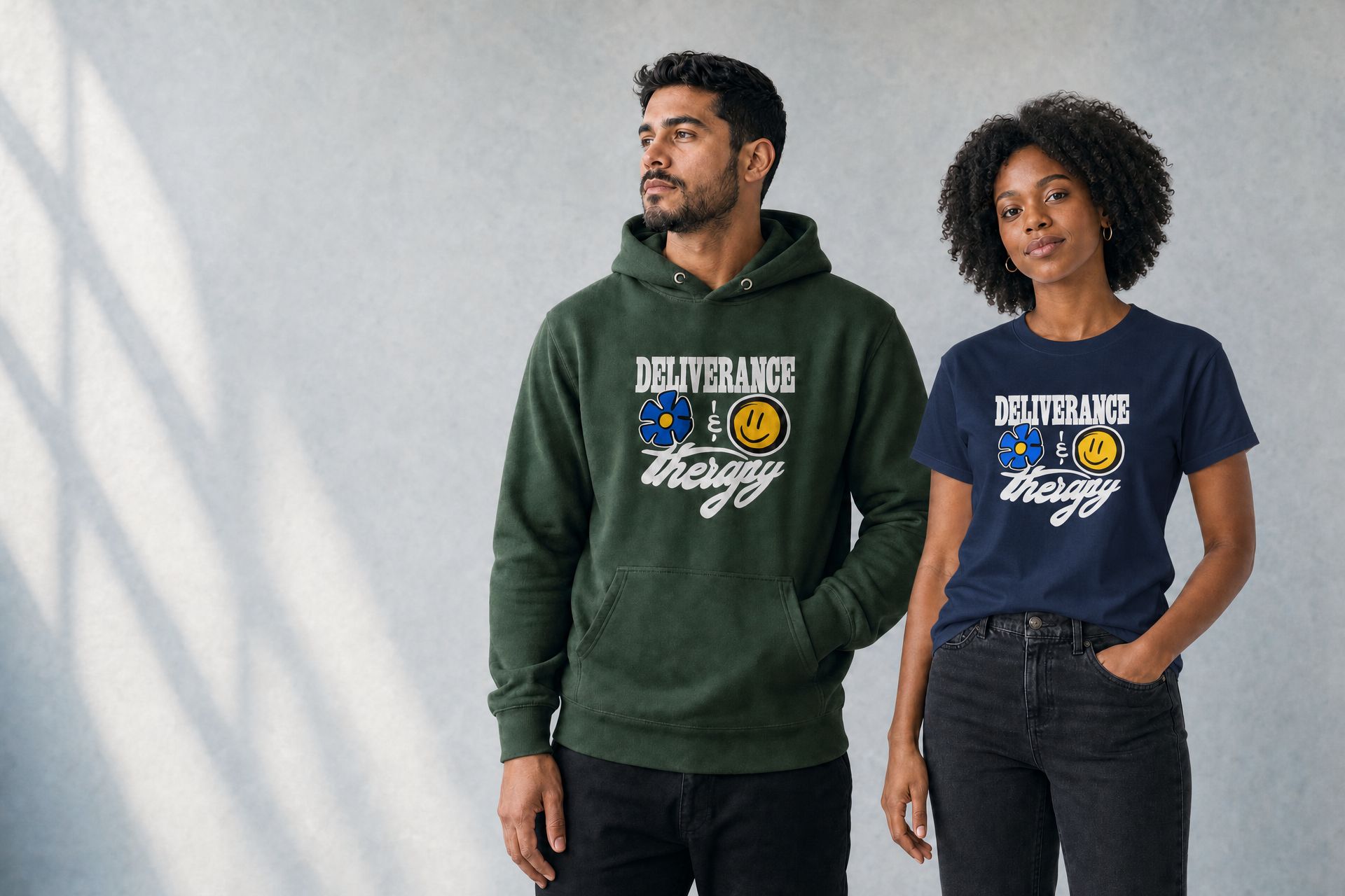Man in the forest green Deliverance and Therapy emoji hoodie and woman in the navy emoji tee